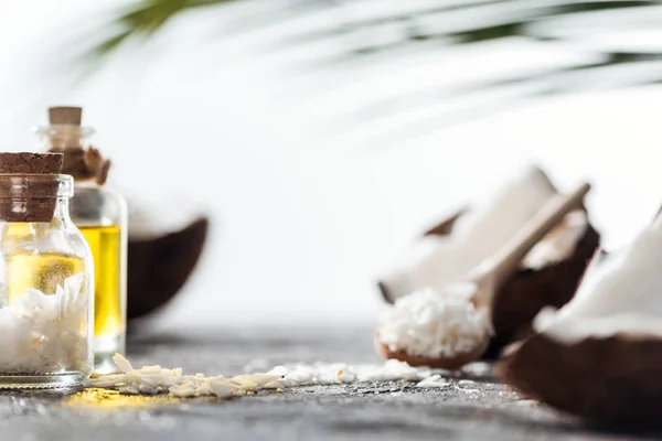 Selective focus of bottle with coconut shaving and cork near cracked coconuts and oil — Stock Photo