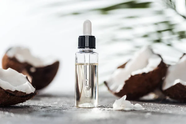 Selective focus of glass bottle with coconut serum and dropper near cracked coconuts — Stock Photo