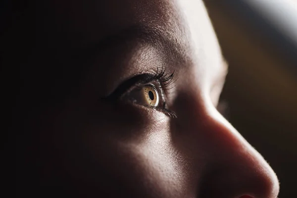 Vista de perto do olho de mulher jovem com pestanas e sobrancelha olhando para longe no escuro — Fotografia de Stock