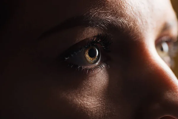 Крупный план глаза взрослой женщины, глядящей вдаль в темноте — стоковое фото