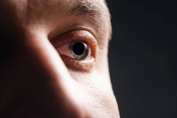 Close up view of adult man eye with eyelashes and eyebrow looking away isolated on black — Stock Photo