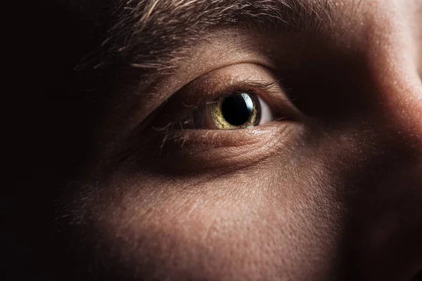 Vista de cerca del ojo del hombre adulto mirando hacia otro lado en la oscuridad - foto de stock