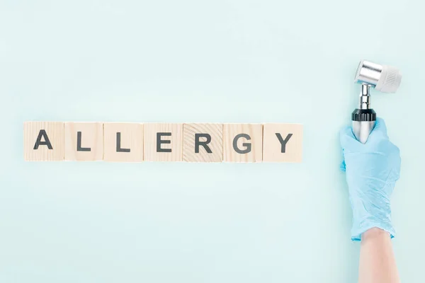 Cropped view of doctor holding dermatoscope near wooden blocks with allergy inscription isolated on blue — Stock Photo