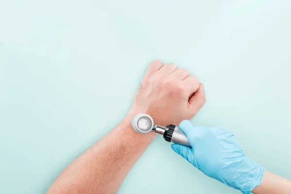 Cropped view of doctor examining hand of man with dermatoscope isolated on blue — Stock Photo