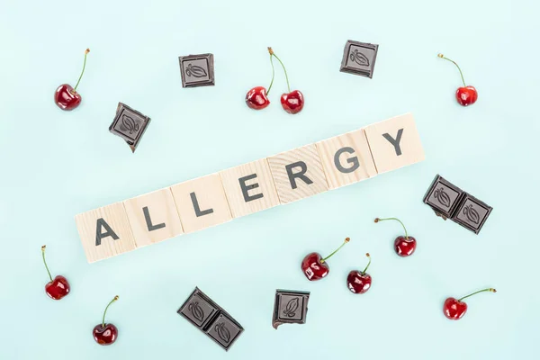 Top view of wooden blocks with allergy lettering near cherries and chocolate isolated on blue — Stock Photo