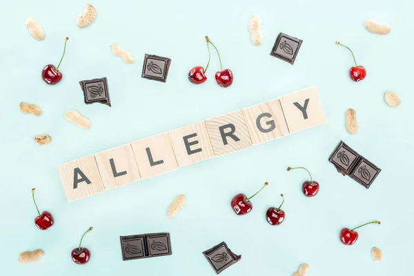 Top view of wooden blocks with allergy lettering near cherries, nuts and chocolate isolated on blue — Stock Photo