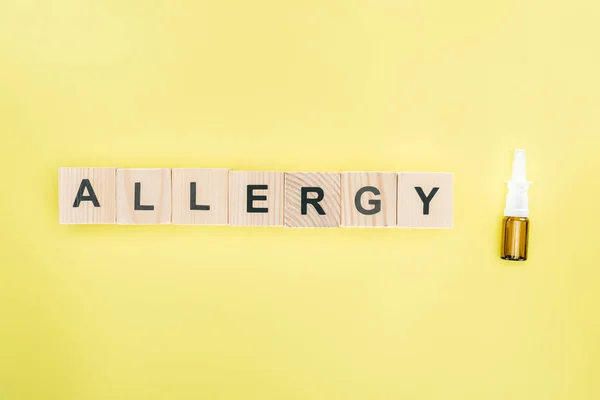 Ansicht von Holzblöcken mit Allergie-Schriftzug in der Nähe von Nasenspray isoliert auf gelb — Stockfoto
