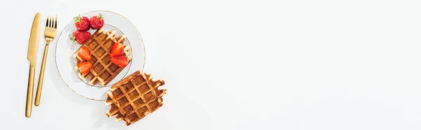 Panoramic shot of cutlery near waffles with strawberries on plate on white — Stock Photo