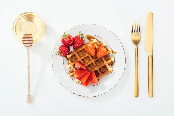 Vista superior de waffle com morangos na placa perto de talheres, tigela com mel e mergulhador de madeira — Fotografia de Stock