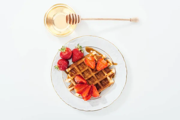 Top view of bowl with honey and wooden dipper near plate with waffle and strawberries on white — Stock Photo