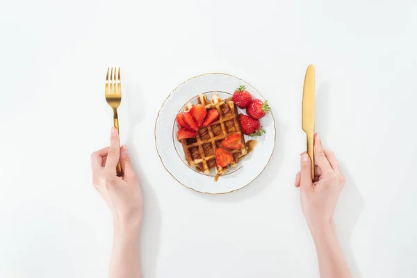 Cropped view of woman holding fork and knife near plate with waffle and strawberries on white — Stock Photo