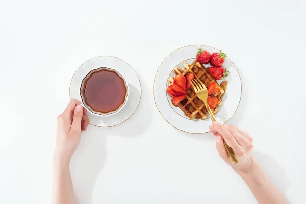 Vista recortada de la mujer sosteniendo la taza con té y tenedor en blanco - foto de stock