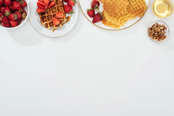 Vista superior de gofres y fresas en cuencos plateados cerca con miel y nueces en blanco - foto de stock