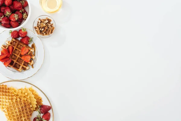 Vista superior de waffles saborosos e morangos em banhado perto de tigelas com mel e nozes em branco — Fotografia de Stock