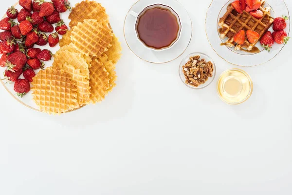 Vista superior de gofres, fresas, miel, nueces y té sobre blanco - foto de stock