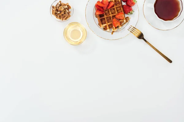 Top view of bowls with nuts and honey near tea and plate with waffles on white — Stock Photo