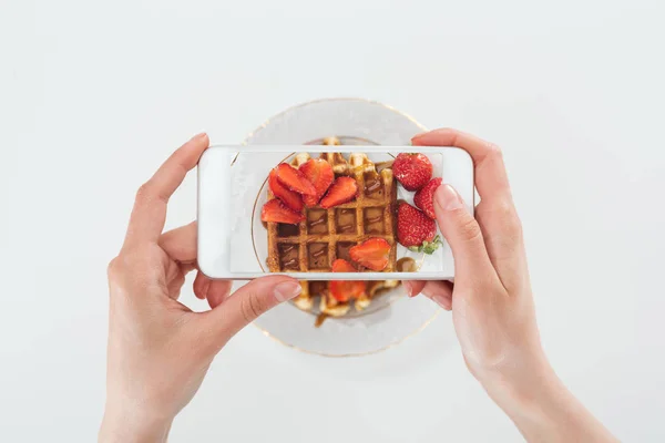 Vista cortada o mulher tirar foto de waffle saboroso com morangos na placa isolada em branco — Fotografia de Stock
