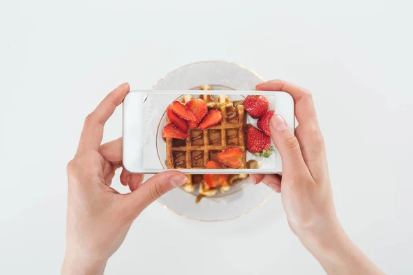 Vista recortada o mujer tomando foto de sabroso gofre con fresas en plato aislado en blanco - foto de stock