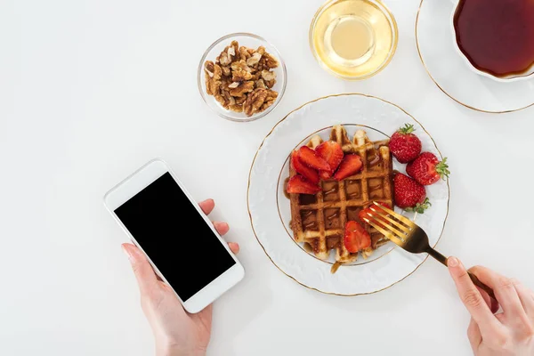 Cropped view of woman eating breakfast and holding smartphone on white — Stock Photo