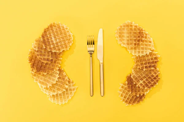 Vista superior de gofres cerca de tenedor dorado y cuchillo en amarillo - foto de stock