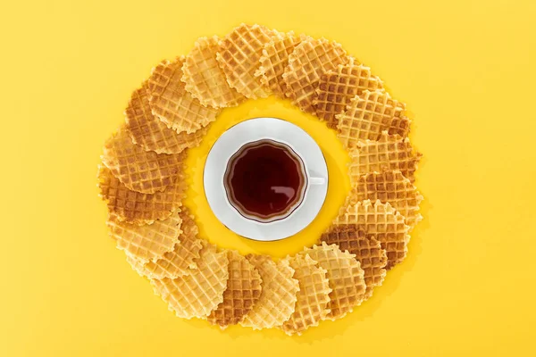 Draufsicht auf Waffeln im Kreis mit Tasse Tee in der Mitte auf gelb — Stockfoto