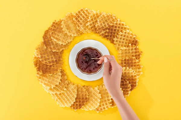 Cropped view of woman holding teapot in cup of tea rounded by waffles on yellow — Stock Photo