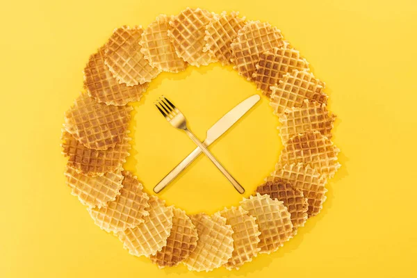 Верхний вид вафель в круге с вилкой и ножом в середине на желтый — стоковое фото