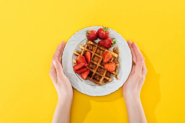 Vue recadrée de la femme tenant la plaque avec gaufre et fraises sur jaune — Photo de stock