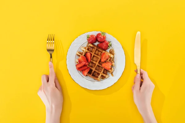 Vista cortada de mulher segurando talheres perto de waffle na placa no amarelo — Fotografia de Stock