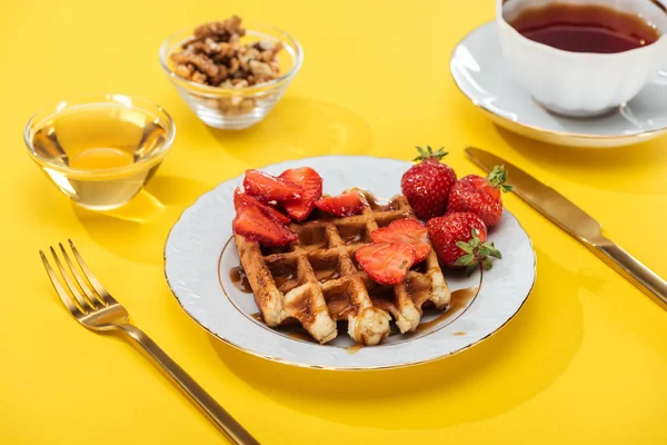 Served breakfast with waffle, strawberries, honey, nuts and tea on yellow — Stock Photo