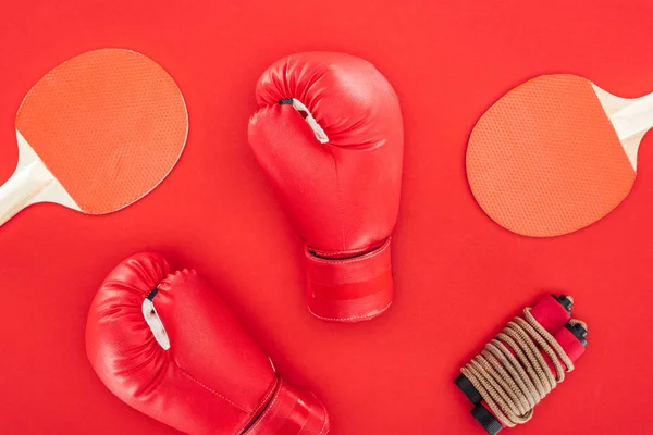 Top view of boxing gloves near ping pong rackets near skipping rope isolated on red — Stock Photo