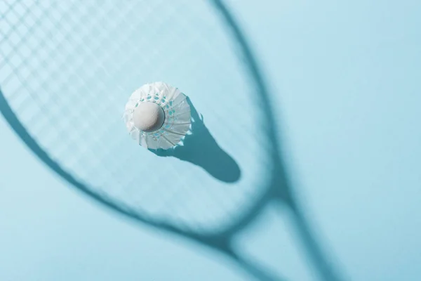 Federball mit weißen Federn im Schatten des Federballschlägers auf blau — Stockfoto