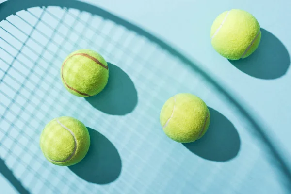 Вид зверху на тенісні м'ячі біля тіні тенісної ракетки на синьому — стокове фото