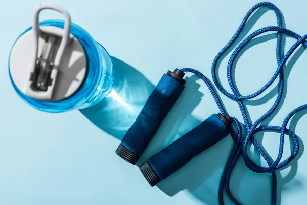 Vista superior de la botella de deporte con agua cerca de saltar la cuerda en azul - foto de stock