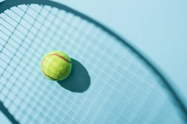 Vue de dessus de balle de tennis près de l'ombre de raquette de tennis sur bleu — Photo de stock