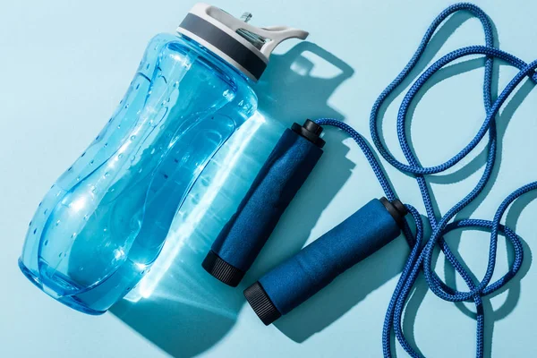 Close up of sport bottle with water near skipping rope on blue — Stock Photo