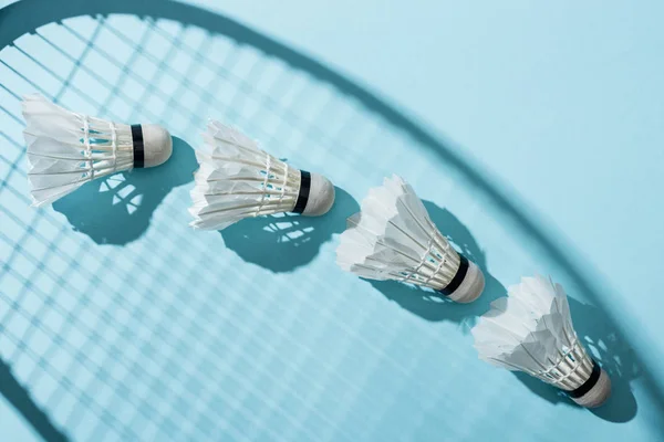 Top view of shuttlecocks near shadow of badminton racket on blue — Stock Photo