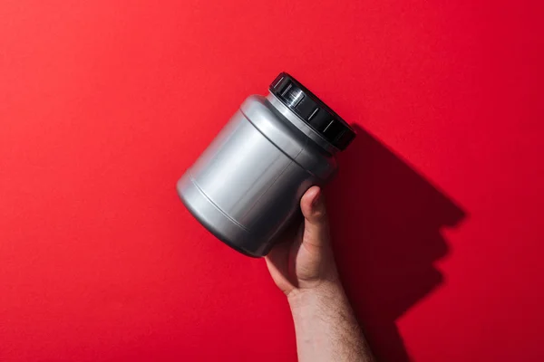 Cropped view of man holding grey jar on red — Stock Photo