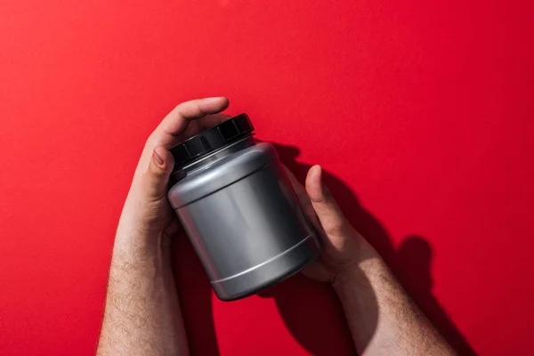 Cropped view of man holding plastic jar in hands on red — Stock Photo