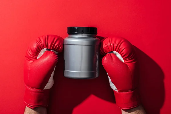 Cropped view of boxer holding grey jar in boxing gloves on red — Stock Photo