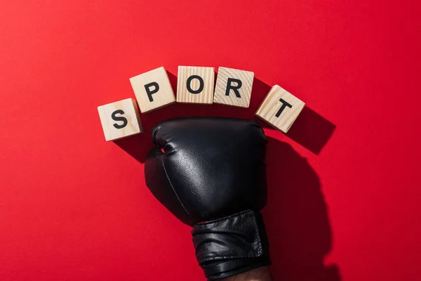 Cropped view of man in boxing glove near wooden cubes with sport lettering on red — Stock Photo