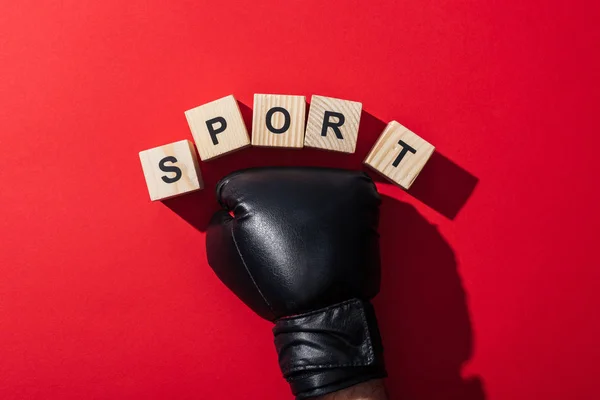 Vue recadrée de l'homme en gant de boxe près de cubes en bois avec lettrage sport sur rouge — Photo de stock