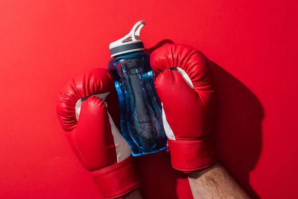 Vista cortada de boxer segurando garrafa esporte com luvas de boxe no vermelho — Fotografia de Stock