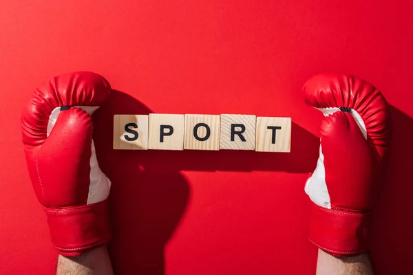 Vue recadrée de l'homme en gants de boxe près de cubes en bois avec lettrage sport sur rouge — Photo de stock