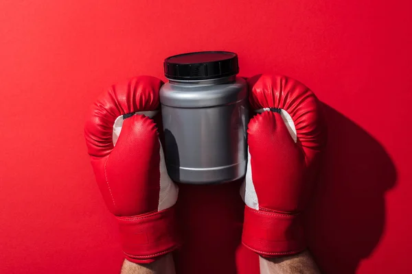 Cropped view of man holding grey jar in boxing gloves on red — Stock Photo