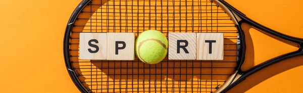 Панорамный снимок деревянных кубов со спортивными надписями возле теннисного мяча и теннисной ракетки на желтом — стоковое фото