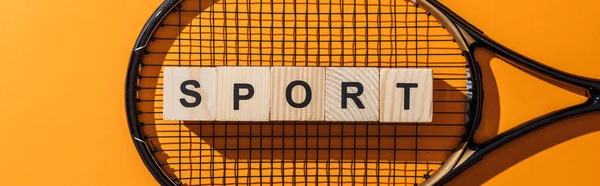 Panoramic shot of wooden cubes with sport lettering near tennis racket on yellow — Stock Photo