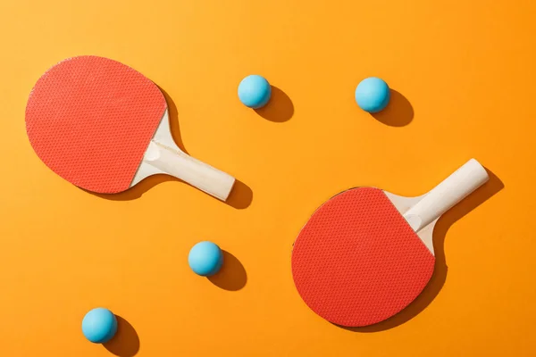 Вид на голубые мячи для пинг-понга рядом с ракетками для настольного тенниса на желтом — стоковое фото