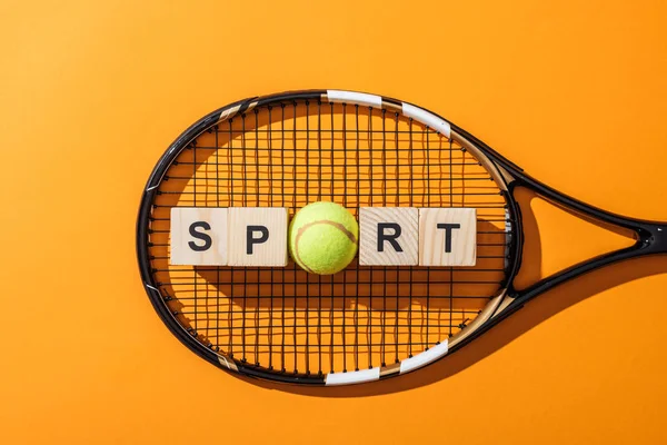 Vista superior de cubos de madeira com letras esportivas perto de bola de tênis e raquete de tênis em amarelo — Fotografia de Stock