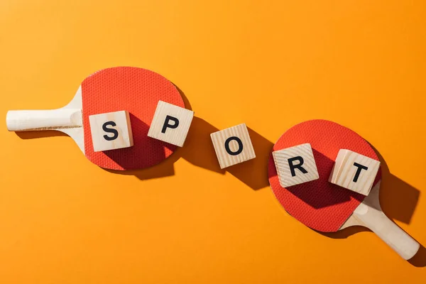 Vista dall'alto di cubi di legno con scritte sportive vicino a racchette da ping pong su giallo — Foto stock